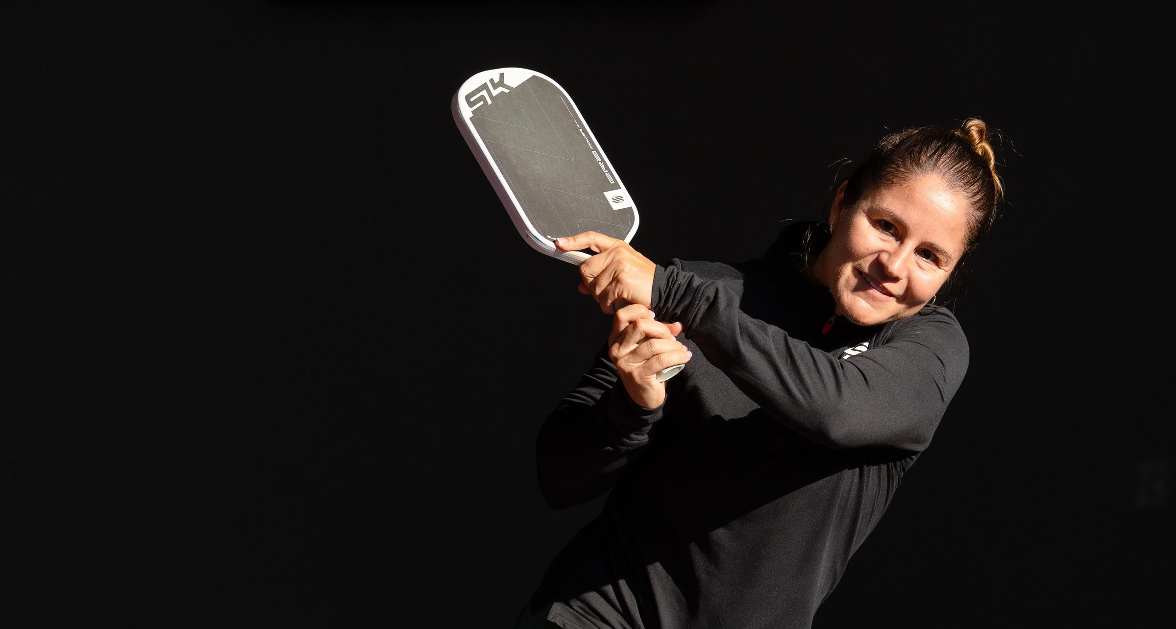 Charlie Treviño following through on a two-handed backhand, Selkirk SLK ERA paddle in hand, lit against a black background